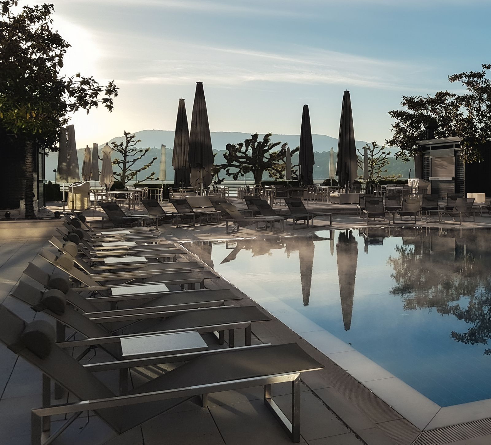 Ruhige Terrassenanlage mit Wasserfl&auml;che und Bergkulisse im Morgenlicht